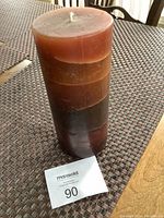 Photo of a cylindrical, multi-layered brown pillar candle measuring approximately 7.5 inches tall on a woven mat surface.