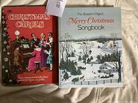 Two books side by side showing front covers: Christmas Carols and The Reader's Digest Merry Christmas Songbook with winter scene.