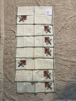 Seven handmade cloth napkins arranged in two columns. Each napkin displays a floral needlepoint design near one corner with green crocheted edges.