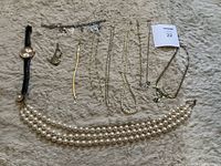 Full view of the lot showing a wristwatch, charm bracelet, gold-tone bangle, several chain necklaces, and multiple strands of pearl necklaces all laid flat on a fuzzy surface.