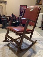 Side view of the vintage folding rocking chair showing wooden frame, brown vinyl cushioned seat and backrest, and curved rockers.