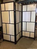 Two-panel IKEA RISÖR room divider with black frame and white panels showing a geometric pattern.