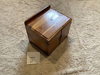 Wooden jewelry box shown from above at an angle to display top and one side, sitting on carpet.