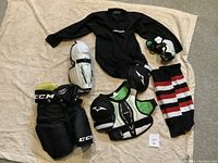 Complete hockey gear set showing pants, shin guards, elbow pads, base layer shirt, and hockey socks.