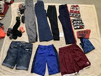 All items laid out on a beige floor showing pants, shorts, socks, and beanies.