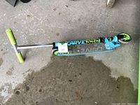 Kid's kick scooter lying on concrete floor, showing the full scooter from side angle with the handlebar, deck, and wheels.