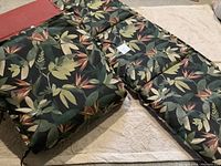 Photo of three rectangular patio lounge cushions with a tropical leaf and floral pattern, laid out on a light surface.