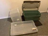 Photo showing three large plastic storage bins: one translucent with a snap-tight lid, one green with an open hinged lid, and one tall translucent bin turned on its side.