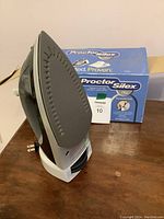 Side view of the Proctor Silex nonstick soleplate steam iron standing upright next to its box