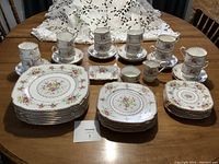 Overview of 8 settings dinnerware, tea cups, saucers, and small serving pieces arranged on table