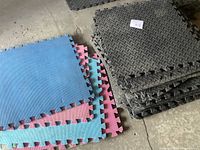 Stack of black and colored interlocking rubber mats arranged on floor. Colors include blue, pink, purple mats with black mats.