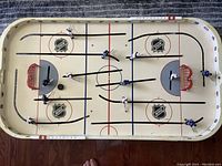 Full overhead shot of the table top hockey game, showing playing surface with NHL logos, player figures on rods and goals.