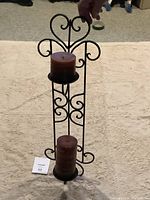 Full view of black metal wall sconce with two brown pillars candles vertically mounted on holder with decorative scrollwork.