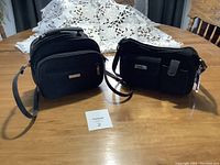 Two black women's purses displayed on wooden table, showing fronts and straps