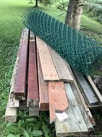 Stack of assorted wood boards and green vinyl-coated chain link roll on top, showing the length and condition of boards and fencing.