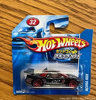 Front view of sealed Hot Wheels die-cast toy car in packaging. The car is a black Acura NSX with red wheels and racing decals.