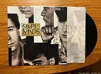Front of Simple Minds album cover "Once Upon A Time" with black and white collage of band members and visible vinyl record in plastic sleeve.