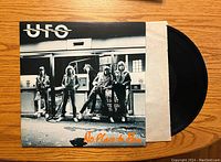 Front cover of UFO No Place to Run vinyl album showing band members at a gas station in black and white with orange album title.