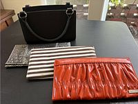 Basic black handbag with three separate magnetic covers laid in front, showing crocodile print, stripes, and orange ruched styles