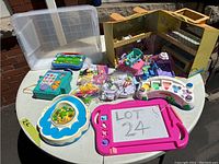 Wide angle photo showing assortment of children's toys including a foldable playhouse, shape sorting toy, various small furniture toys, and other educational toys arranged on a white table.