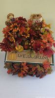 Front view of autumn decor arrangement in wooden box featuring scarecrow dolls, fall flowers, foliage, and decorative sign.