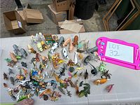 Overview image of small to medium-sized plastic animal figures arranged on a table including farm animals, dinosaurs, and safari creatures.