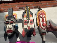 Top view showing all three wooden hand-carved decorative masks laid on ground near brick wall