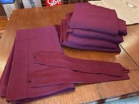 Six folded burgundy blackout drape panels with accompanying fabric ties on a wooden table.