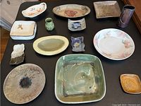 Image showing assorted handmade pottery pieces including dishes, plates, small vases, and figurines arranged on a dark surface.