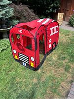 Side view of the red child-sized play fire truck tent showing details such as window mesh, printed fire truck design, and steering wheel inside.
