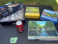 Set of five puzzles on table outdoors, showing four flat box puzzles and a 3D Coca-Cola can puzzle beside them.