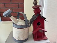 Galvanized metal watering can and red painted wooden bird house with metal roof seen together.