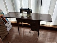 Wooden sewing station with fold-out wings and three drawers, showing the entire setup in a room with wood floor