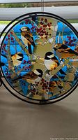 Close-up of stained glass showing six chickadees perched on branches with red berries and snow background.