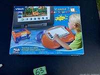 Photo of the VTech VSmile Art Studio digital art system in original box showing product branding, features, and a child using the drawing pad connected to a TV screen.