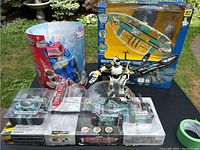 Photo showing Transformer figure in red and blue packaging, Command Force playset with robot figure inside box, and radio controlled airplane in box with yellow background.