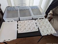 Three clear plastic stackable food containers with snap-on lids and handles shown separated on table with trays in front