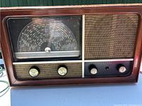 Wooden vintage radio showing upper left front view with three knobs and speaker grille