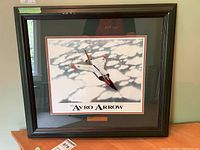 Framed Avro Arrow print with plaque shown hanging on wall. Frame has visible finish damage.