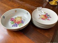 Bowl and plates displaying fruit design motifs with some plates stacked and bowl separate.