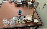 Lot of assorted candle holders on a brown table including metal, glass, and ceramic pieces with a metal candle snuffer.