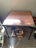 Foldable card table seen from top angle showing surface wear on the tabletop and metal legs folded out.