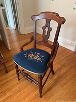 Full view of vintage wooden chair showing carved back, armrests, and floral upholstered seat on blue fabric