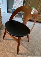 Front angled view showing teak curved backrest and black vinyl seat with visible wear and damage on legs.