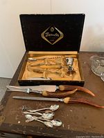 Barmates barware in original box with metallic jigger and stirrer, carving utensils with antler handles, and small collectible spoons on table