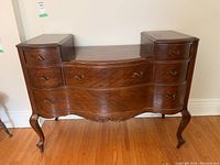 Frontal view of antique wooden dresser showing six drawers and curved design with cabriole legs on casters.