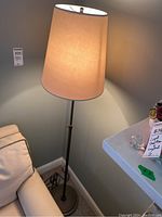 Full view of metal floor lamp with beige fabric lampshade illuminated, placed next to a couch and side table