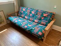 Futon couch with wood frame and patterned green cushion at an angle serving as a couch.