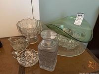 Overall view of the lot showing glassware and crystal items on a wooden surface including the decanter, pedestal bowl, and green glass dish.