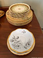 Photo showing stacks of small green and gold decorated dessert plates and larger cream fruit plates with floral patterns